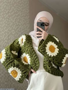 a woman taking a selfie while wearing a green crocheted jacket and white skirt