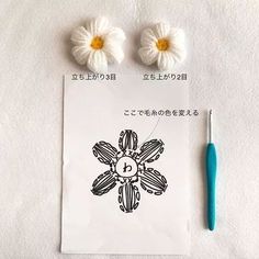 two crocheted flowers sitting on top of a piece of paper next to a pen