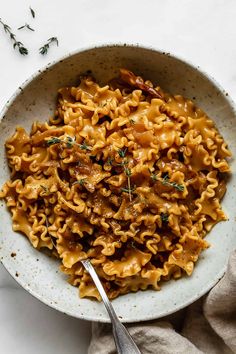 a white bowl filled with pasta and meat on top of a table next to a fork