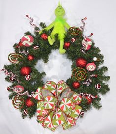 a christmas wreath with ornaments and a green stuffed animal on the top, sitting in front of it