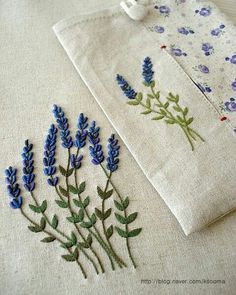 two embroidered napkins with blue flowers on them sitting next to each other, one in front of the other