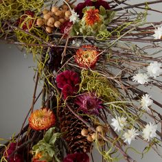 an arrangement of flowers and branches with pine cones