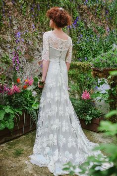 a woman standing in front of flowers wearing a white wedding dress with sheer back and long sleeves