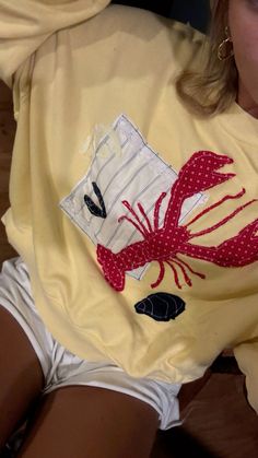 a woman wearing a yellow shirt with a red lobster on it's chest and white shorts