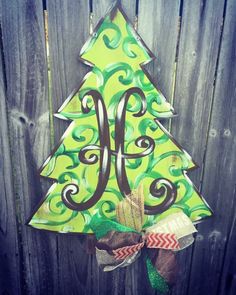 a green christmas tree hanging on the side of a wooden fence with a monogrammed bow