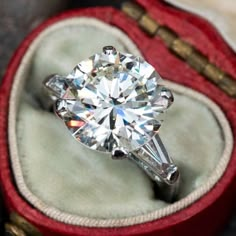 an engagement ring in a red velvet box with its reflection on the diamond inside it