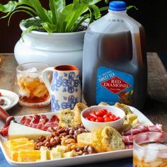 an assortment of meats and cheeses on a platter next to a jug of water