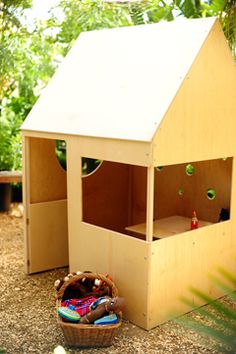 a small wooden house sitting on top of a gravel ground next to a basket filled with toys