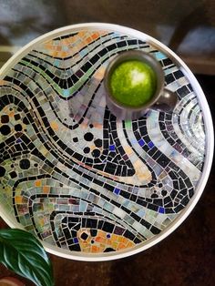 a glass plate with a green ball in it on a table next to a potted plant