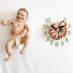 a baby is laying next to a clock with paint all over it's face