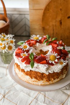 a cake with strawberries and daisies on it sitting on a plate next to flowers