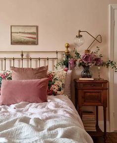 a bed with pink and white pillows on top of it next to a wooden nightstand