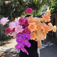 a woman is holding a large bouquet of pink and orange flowers in her hands while walking down the street