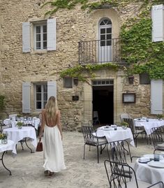 a woman in a white dress is walking through an outdoor dining area with tables and chairs