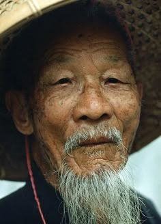 an old man with a white beard wearing a straw hat and looking at the camera