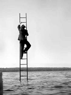 a man standing on top of a ladder next to the ocean with his feet in the water