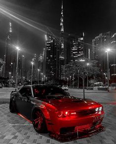 a black and white photo of a red sports car in front of a cityscape