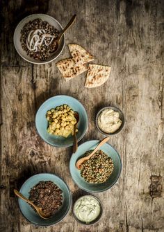 three bowls filled with different types of food on top of a wooden table next to two spoons