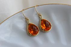 a pair of gold earrings with an orange stone in the center on a white plate