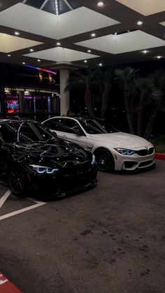 two cars parked in a parking lot next to each other near a building at night