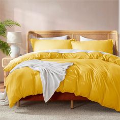 a bed with yellow comforters and pillows in a pink room next to a potted plant