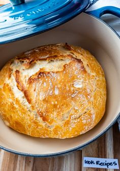 a loaf of bread sitting in a bowl on top of a wooden table next to a blue casserole dish