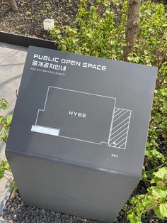 a public open space sign sitting in the middle of some bushes and trees on a sidewalk