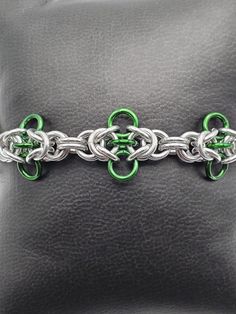 a green and silver chain bracelet on a black leather background with the clasps closed