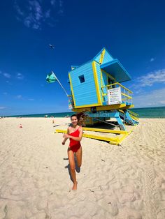 a woman in a red swimsuit running on the beach next to a lifeguard tower