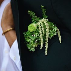 a man wearing a black suit and white shirt holding a boutonniere with green flowers on it