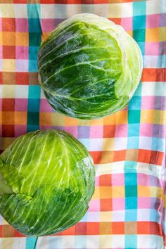 two lettuce heads sitting on top of a checkered cloth covered tablecloth