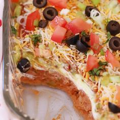 a pizza with cheese, olives, tomatoes and other toppings on it sitting in a pan