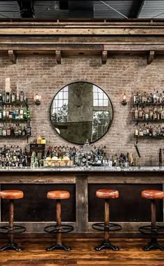 a bar with stools and bottles on the wall behind it in front of a round mirror