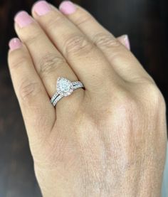 a woman's hand holding a diamond ring on her left hand, with the other hand in front of her