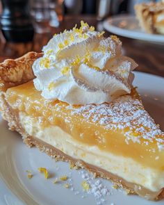 a slice of lemon pie on a white plate with whipped cream and powdered sugar