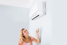 a woman is pointing at an air conditioner on the wall