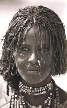 an african woman with dreadlocks and necklaces on her face, looking at the camera