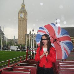 a woman standing in the rain holding an umbrella and looking at her cell phone with big ben in the background