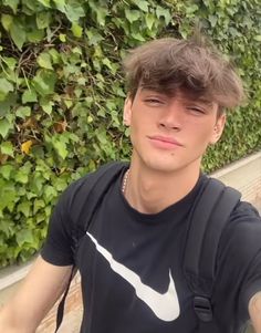 a young man is taking a selfie in front of a wall with green plants