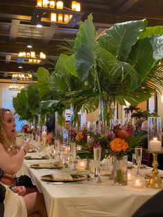 a woman sitting at a table in front of a plant filled centerpiece with candles