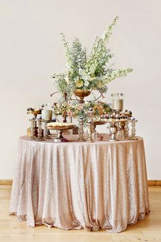 a table topped with lots of desserts and flowers on top of a white table cloth