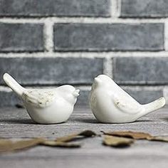 two white ceramic birds sitting next to each other on the ground in front of a brick wall