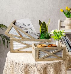 a wooden box filled with donuts sitting on top of a table next to a potted plant