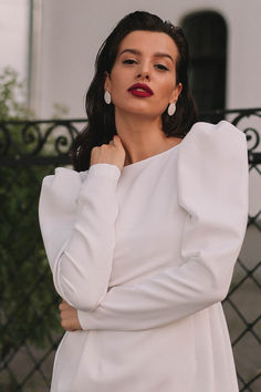 a woman wearing a white dress and red lipstick standing in front of a black fence