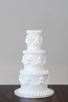 a three tiered white wedding cake sitting on top of a wooden table