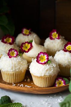 small cupcakes with white frosting and pink flowers on a wooden platter