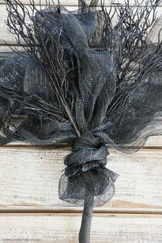 a black bouquet with branches and netting on it sitting on a wooden table next to a wall