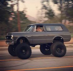 a gray truck with big tires driving down the street