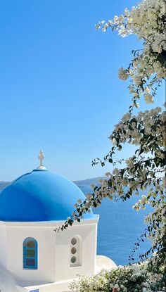 a white and blue building with a cross on it's roof next to the ocean