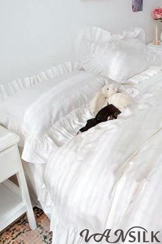 a white bed with ruffled sheets and a stuffed animal on the bottom half of it